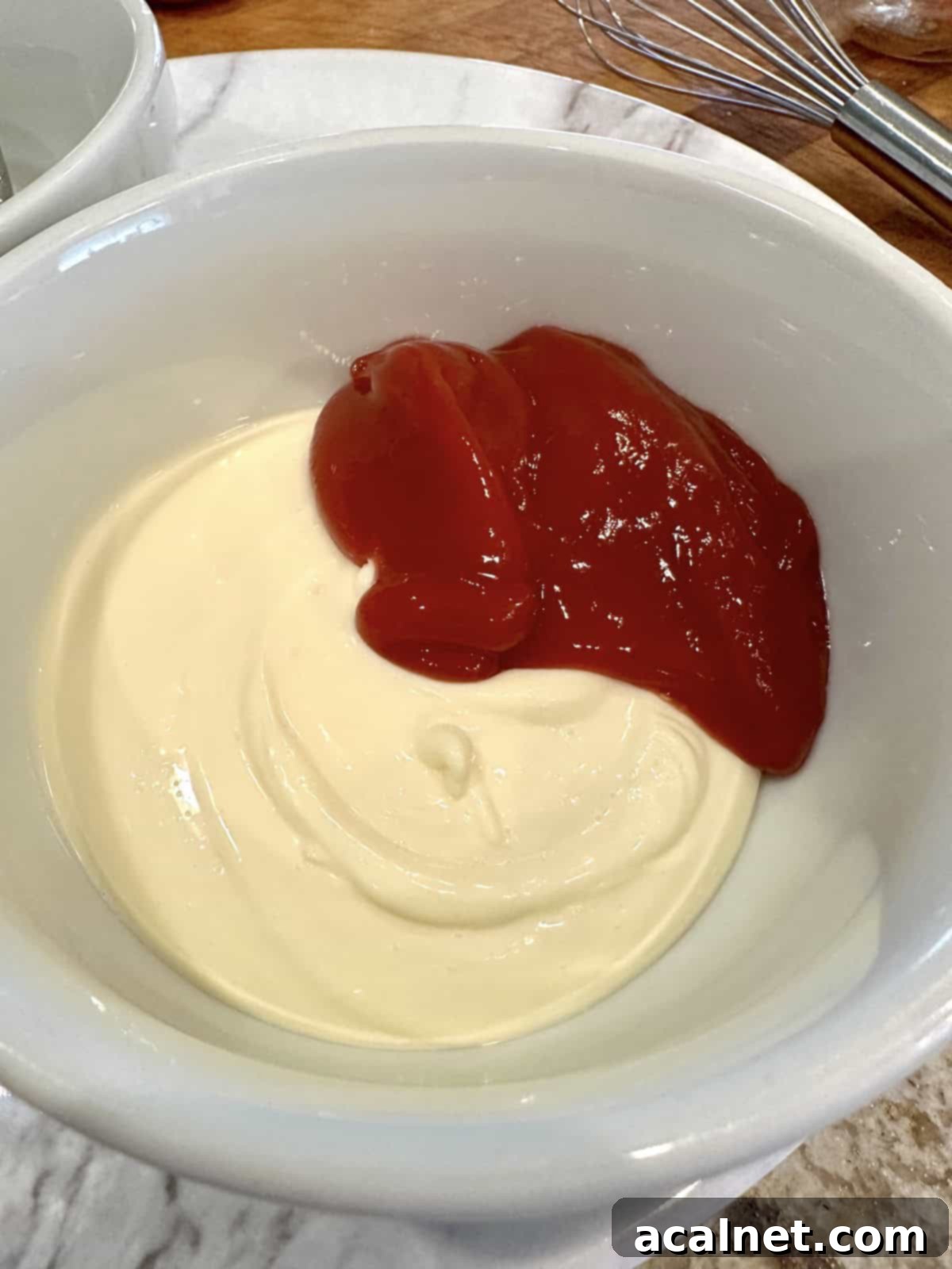 Ultimate Fry Dip 5 A small glass bowl containing a generous amount of creamy white mayonnaise and a dollop of bright red ketchup, side by side, before mixing.