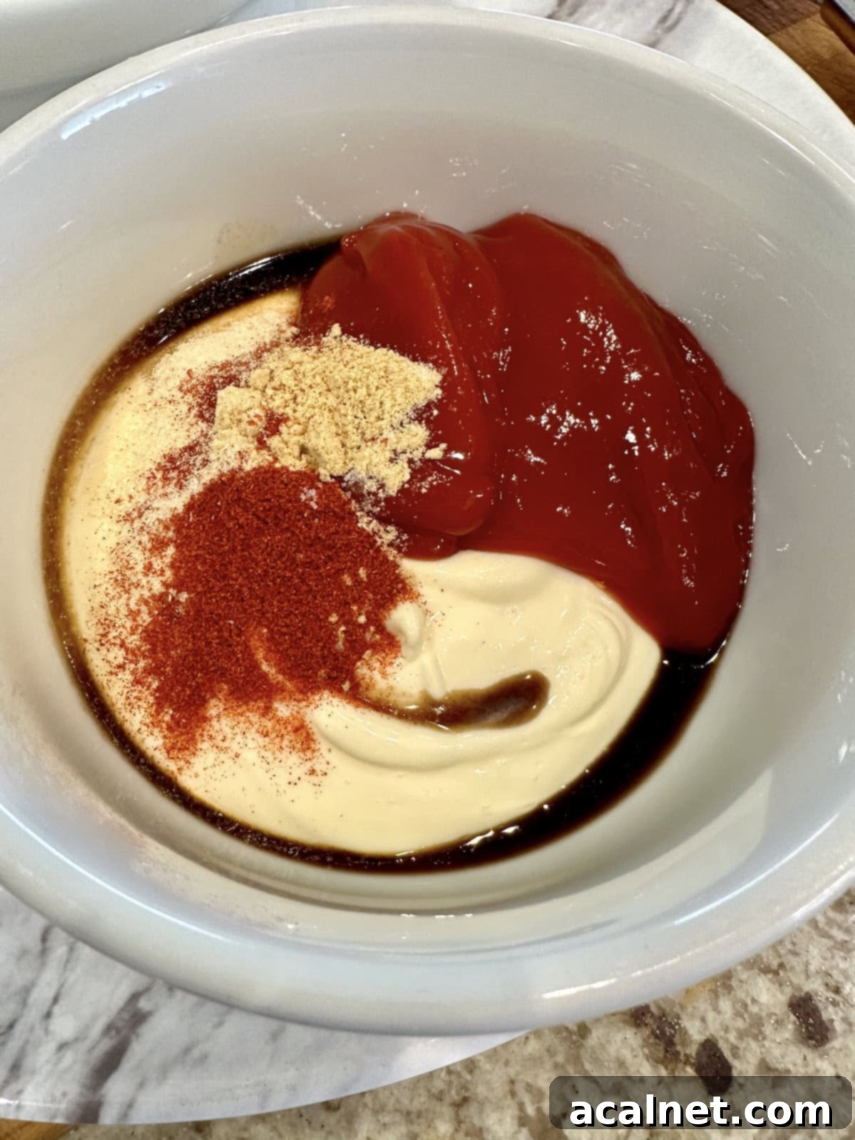 Ultimate Fry Dip 6 All the French fry sauce ingredients, including mayonnaise, ketchup, and various spices like smoked paprika and ground mustard, are in a bowl but not yet blended. The separate colors and textures are visible.