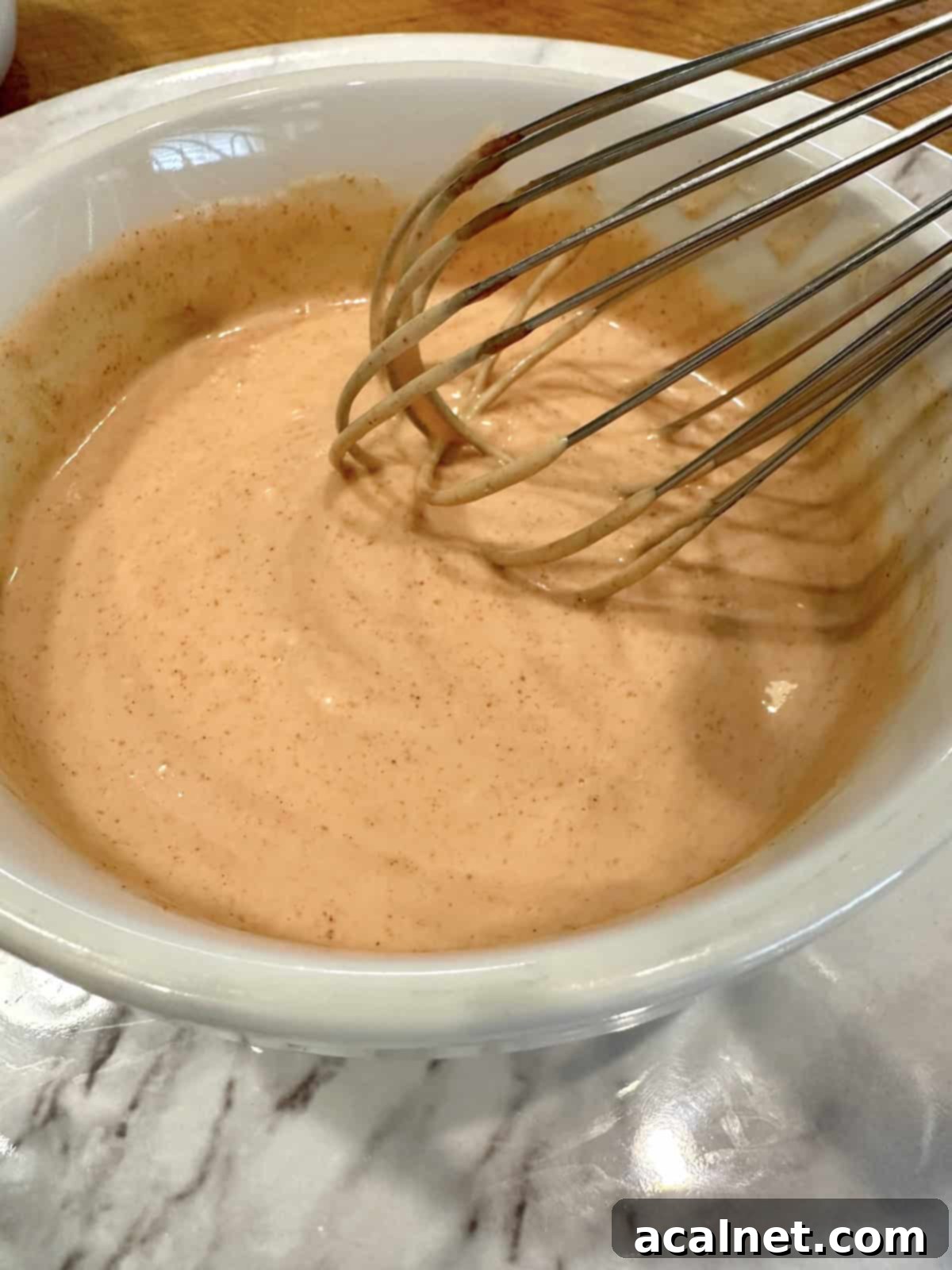 Ultimate Fry Dip 7 A bowl of French fry sauce being vigorously whisked with a metal whisk, showing the ingredients blending into a smooth, creamy, light pink mixture.
