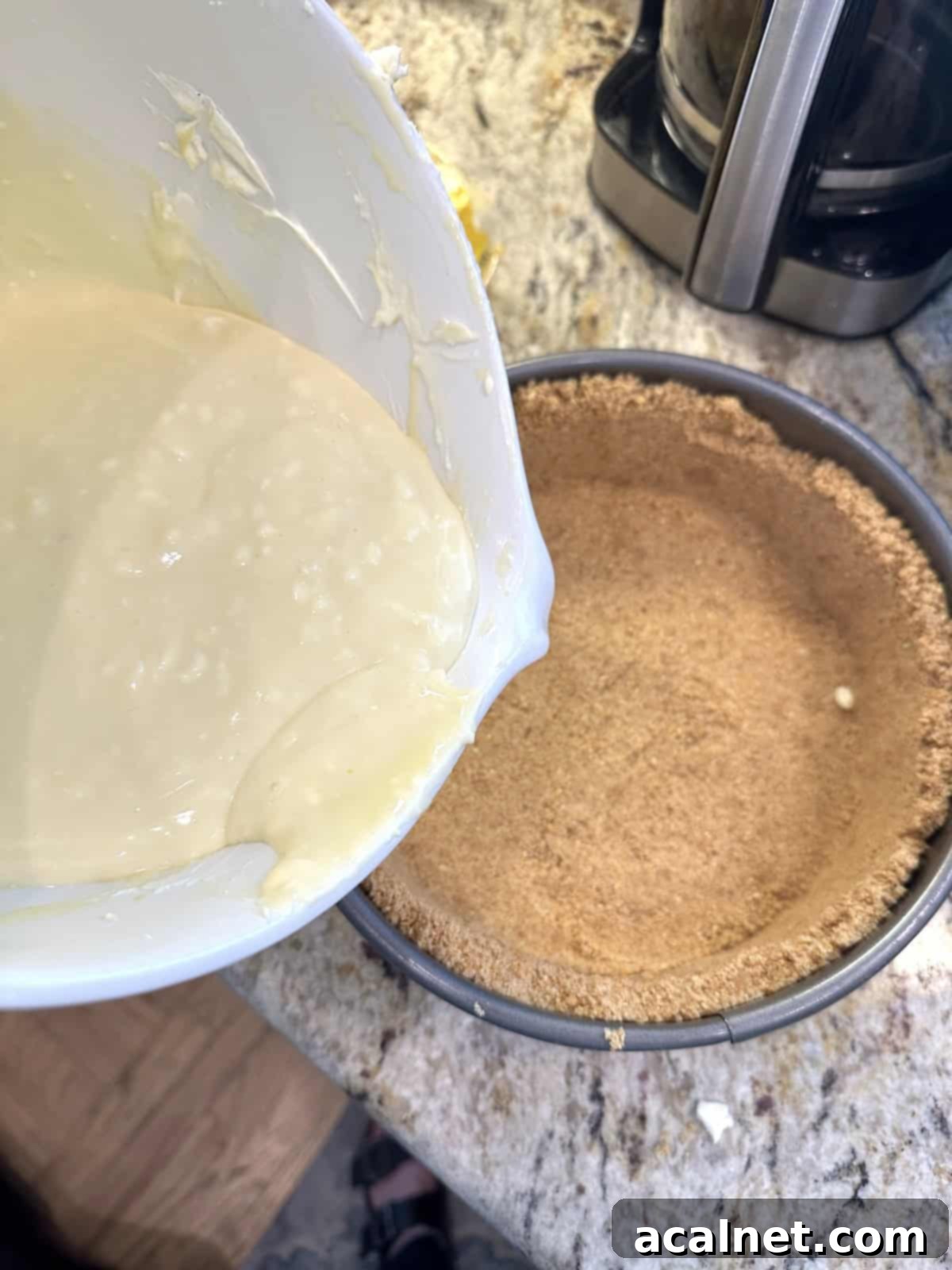 A large mixing bowl filled with the smooth, creamy vanilla cheesecake filling, positioned directly over the perfectly pressed graham cracker crust inside a springform pan, ready for assembly.