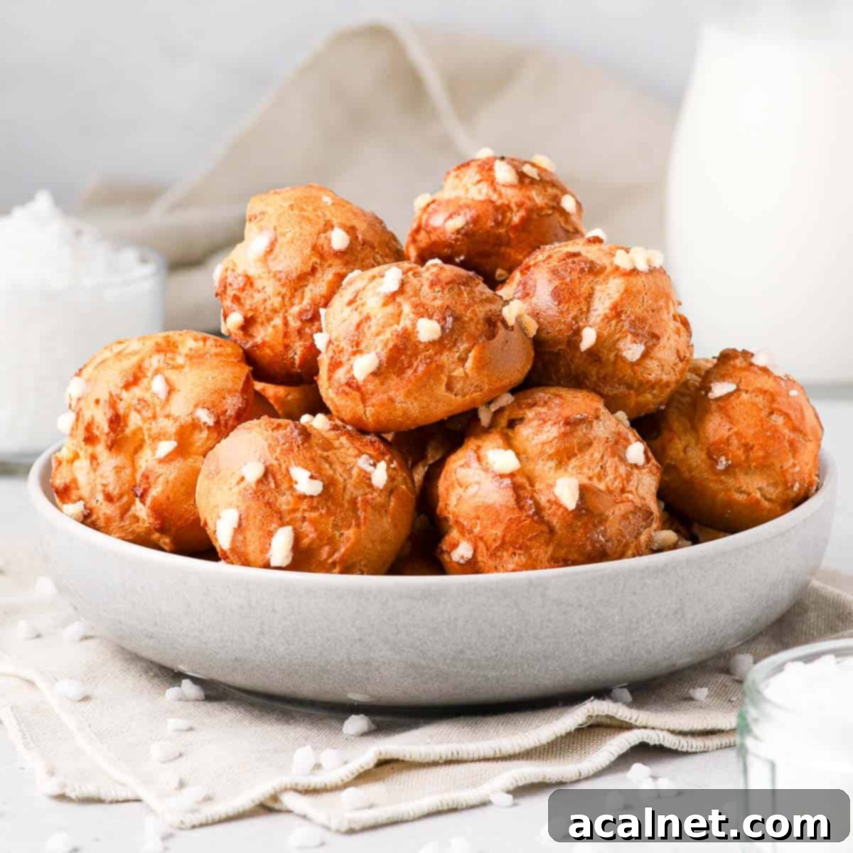 Chouquettes stacked in a grey bowl, highlighting their golden-brown exterior and pearl sugar topping.