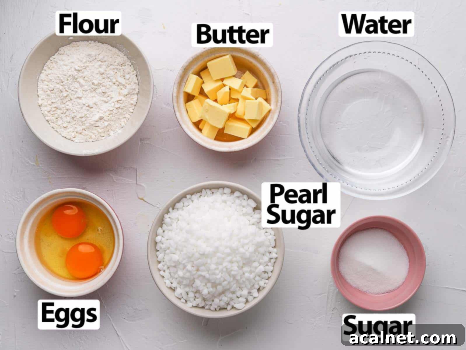 A selection of chouquettes ingredients laid out on a white surface, including butter, eggs, flour, and pearl sugar.