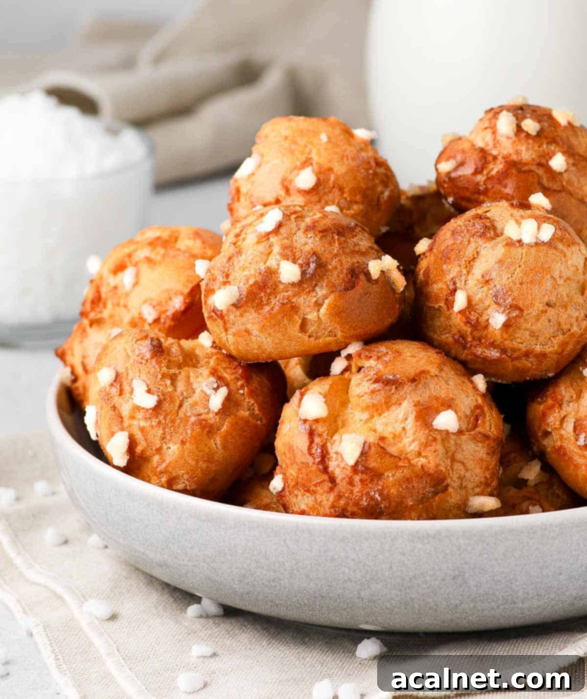 A side view of golden-brown chouquettes, generously topped with pearl sugar, nestled in a grey bowl.