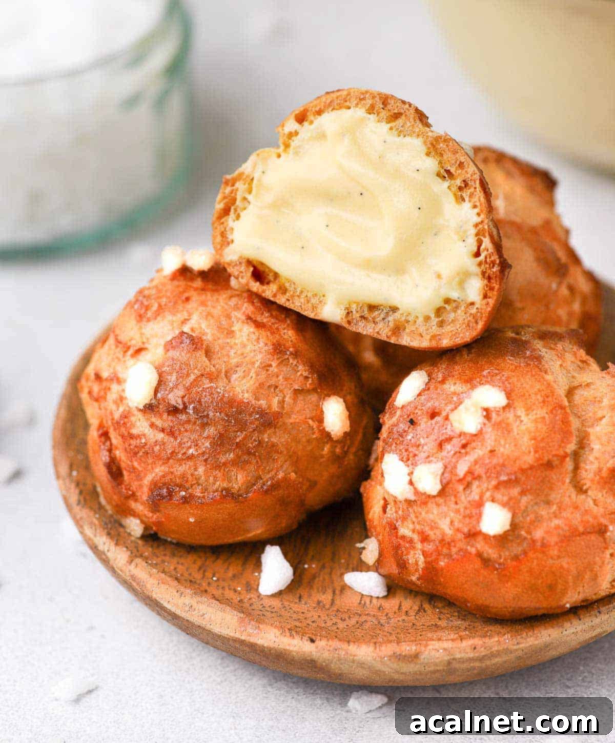 One chouquette sliced in half and filled with cream, resting atop other whole chouquettes in a grey bowl.