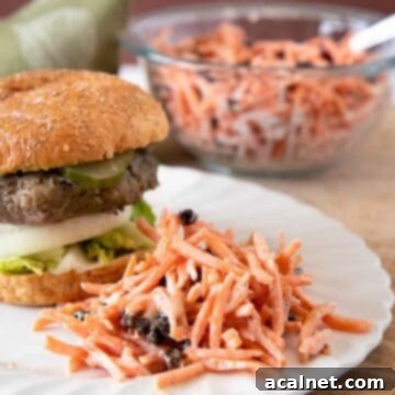 A classic Carrot Raisin Salad served on a plate next to a hamburger, showcasing it as a perfect side dish.