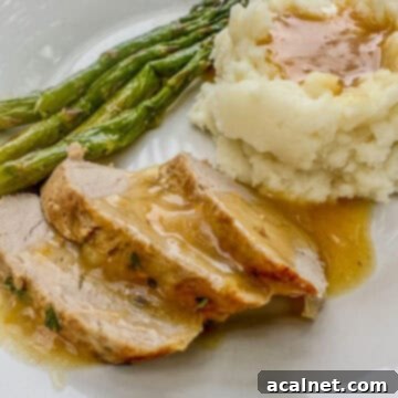 A serving of sliced pork tenderloin with orange sauce on a plate with mashed potatoes and asparagus.