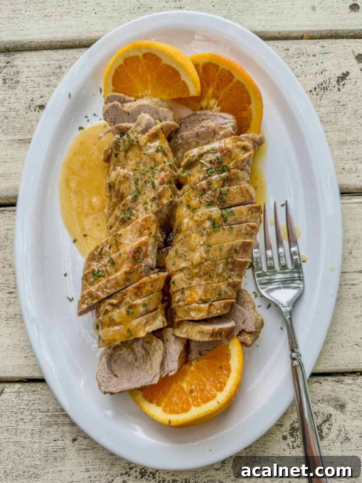 Orange glazed pork tenderloin slices on a serving plate with sliced oranges.