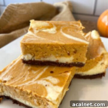 Three perfectly cut marbled pumpkin cheesecake bars, stacked elegantly on a white plate.