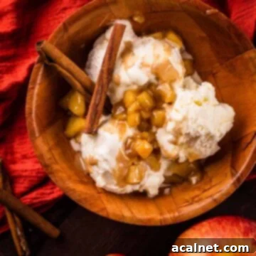 A bowl of creamy vanilla ice cream generously drizzled with homemade caramel apple sauce, with cinnamon sticks as garnish.