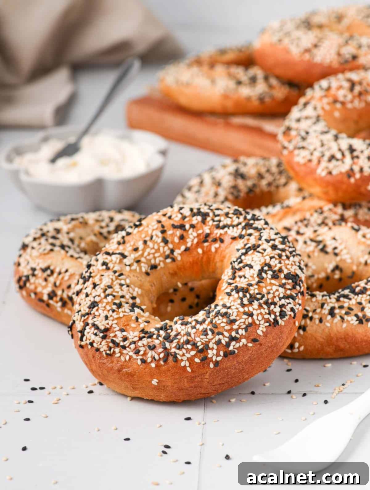 Several homemade sesame bagels stacked on a white tiled surface.