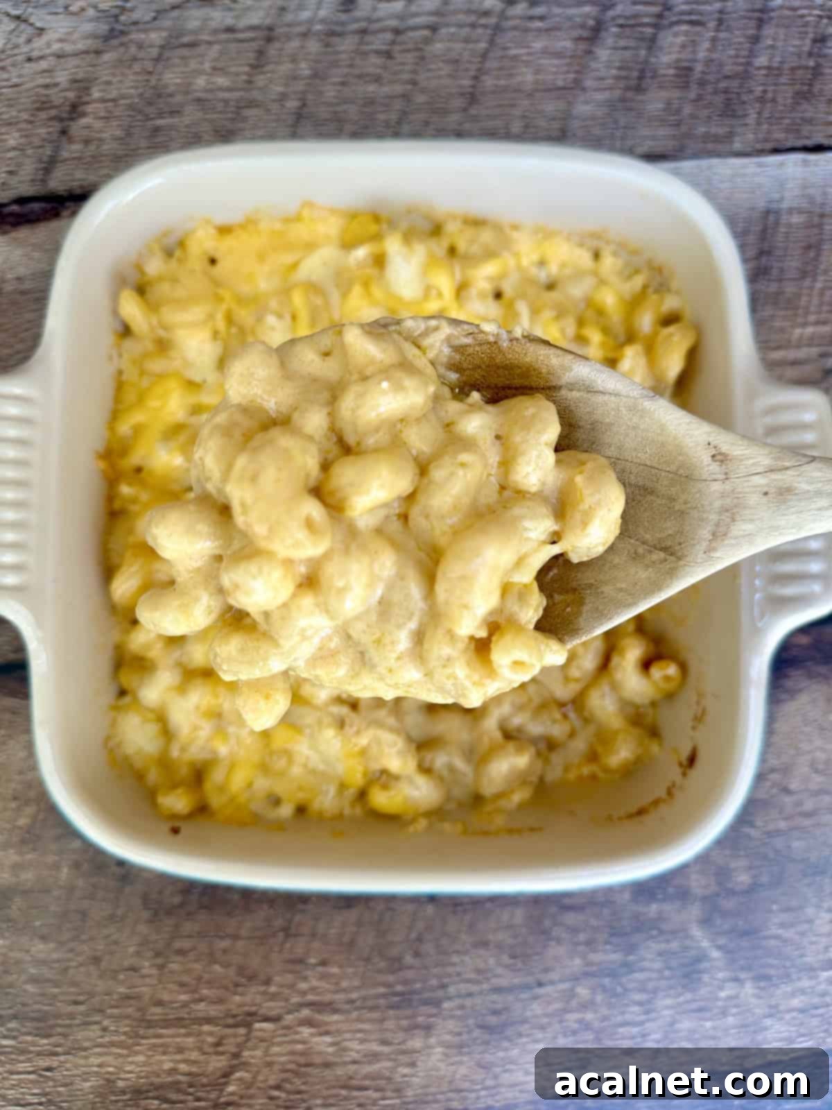 A wooden spoon dishing up a serving a smoked gouda mac and cheese from a baking dish.