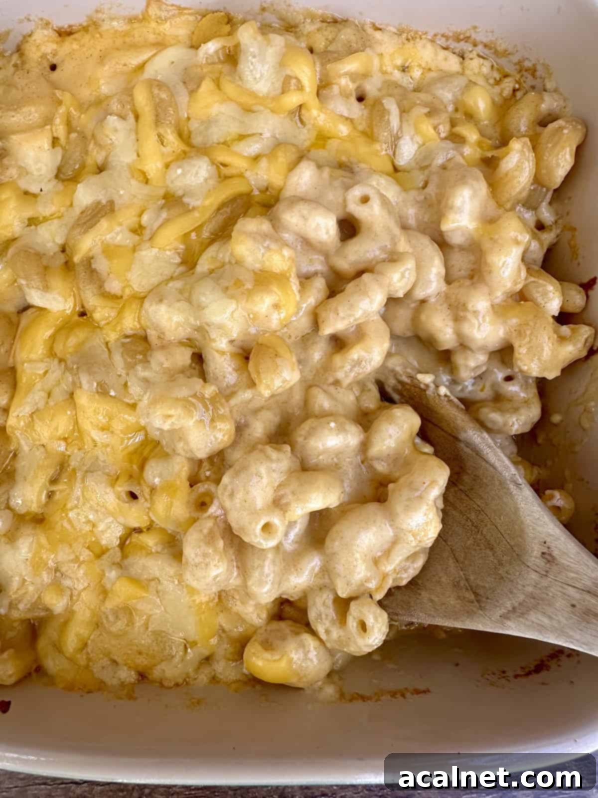 A wooden spoon scooping a serving of smoked gouda mac and cheese from a baking dish.