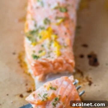 A fork holding a succulent wedge of lemon butter salmon, garnished with fresh herbs and a lemon slice.
