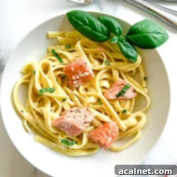 A bowl of creamy fettuccine Alfredo topped with flaky salmon and fresh basil, ready to be enjoyed.
