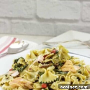 A generous plate of Mediterranean salmon pasta, with tender salmon, colorful vegetables, and a spoon ready for serving.