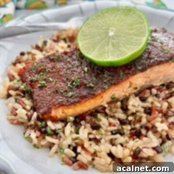 A vibrant piece of baked jerk salmon served on a bed of rice, garnished with a fresh lime wedge.