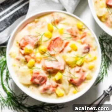 A comforting bowl of creamy salmon chowder, garnished with fresh herbs and served with a spoon.