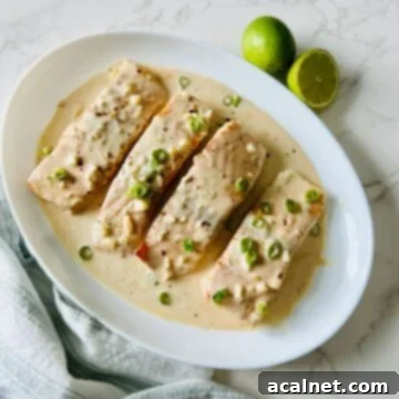 A large plate showcasing creamy salmon in coconut lime garlic sauce, garnished with lime wedges and fresh onions.