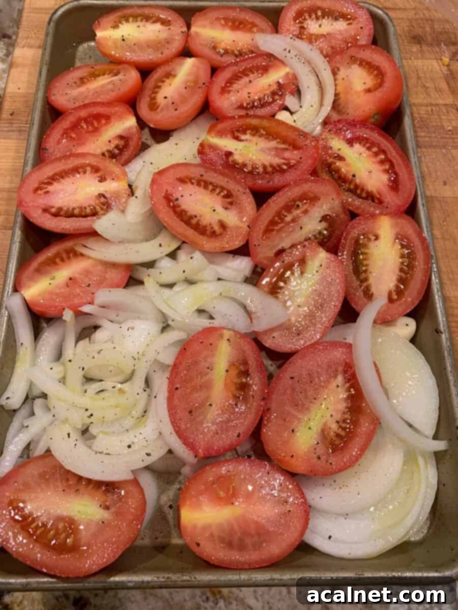 Best Homemade Tomato Basil Soup 3 Halved Roma tomatoes, peeled garlic cloves, and sliced onions arranged neatly on a parchment-lined baking sheet, glistening with olive oil and seasoned, ready for roasting to perfection.