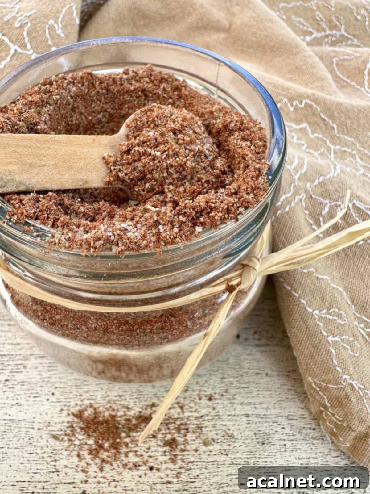 A small jar full of homemade taco seasoning with a spoon on top and a napkin, showcasing the vibrant spice mix.
