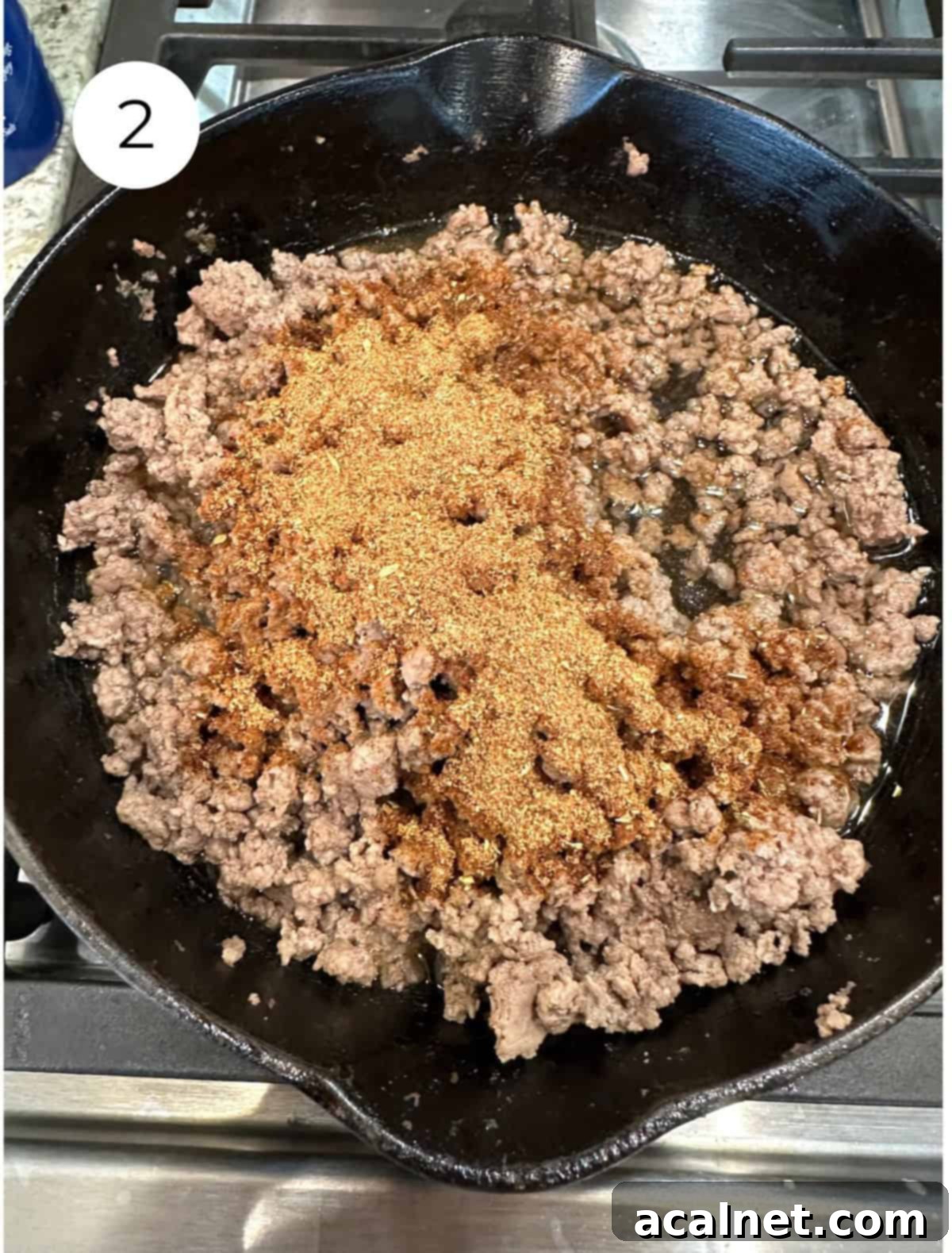 Cooked ground beef with taco seasoning spice being sprinkled into a skillet.