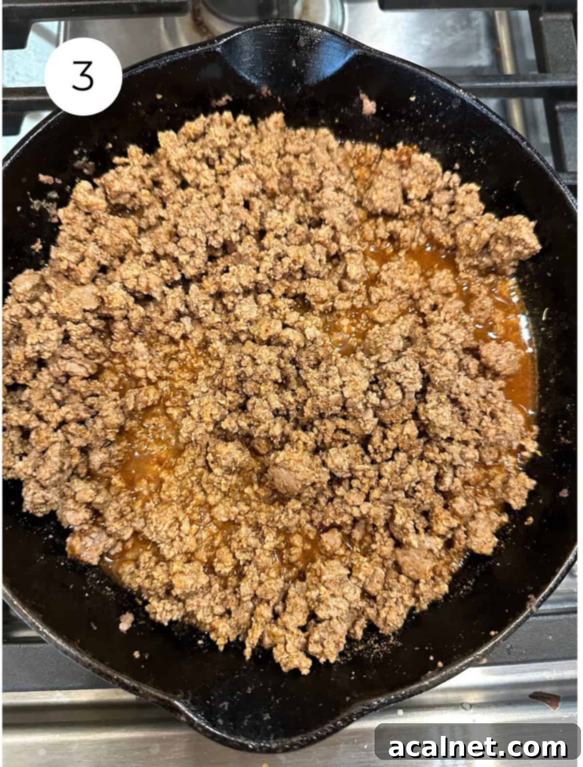 Cooked beef with taco seasoning simmering in a skillet on the stove, absorbing the liquid.
