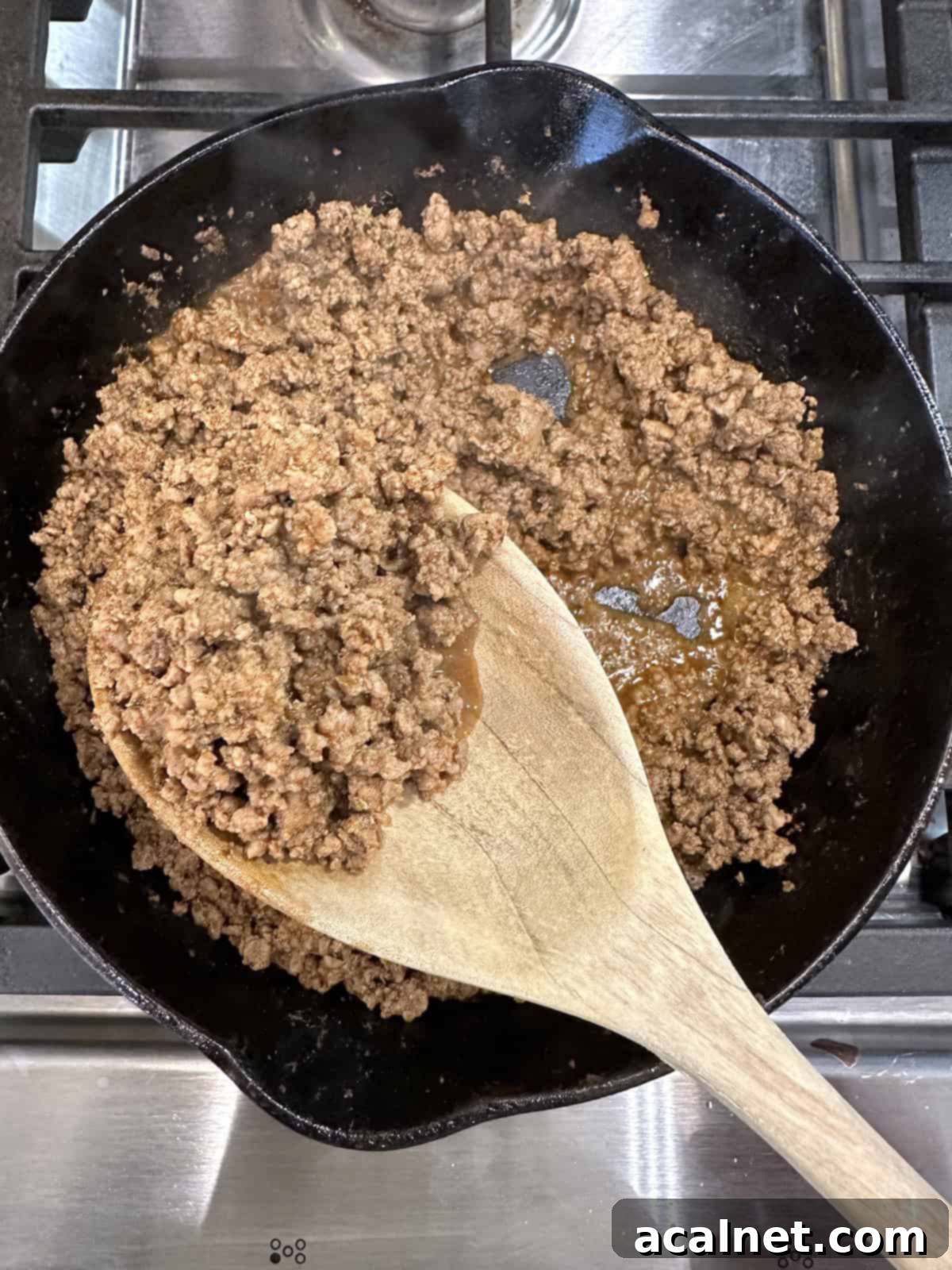Cooked ground beef with taco seasoning in a skillet with a spoon, glistening and ready to serve.