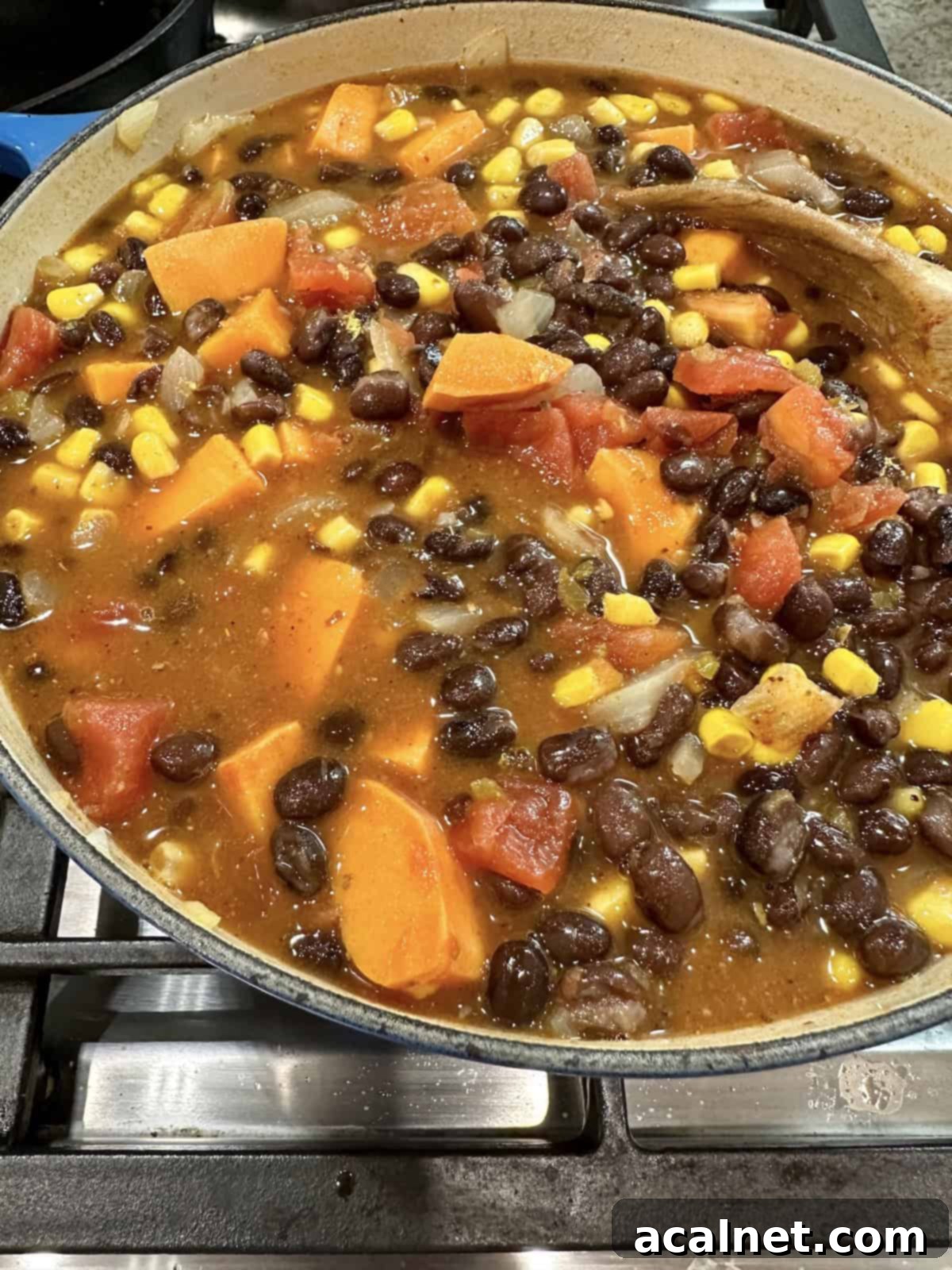 A pot of rich black bean soup with sweet potatoes and corn simmering on the stove, garnished with fresh cilantro.