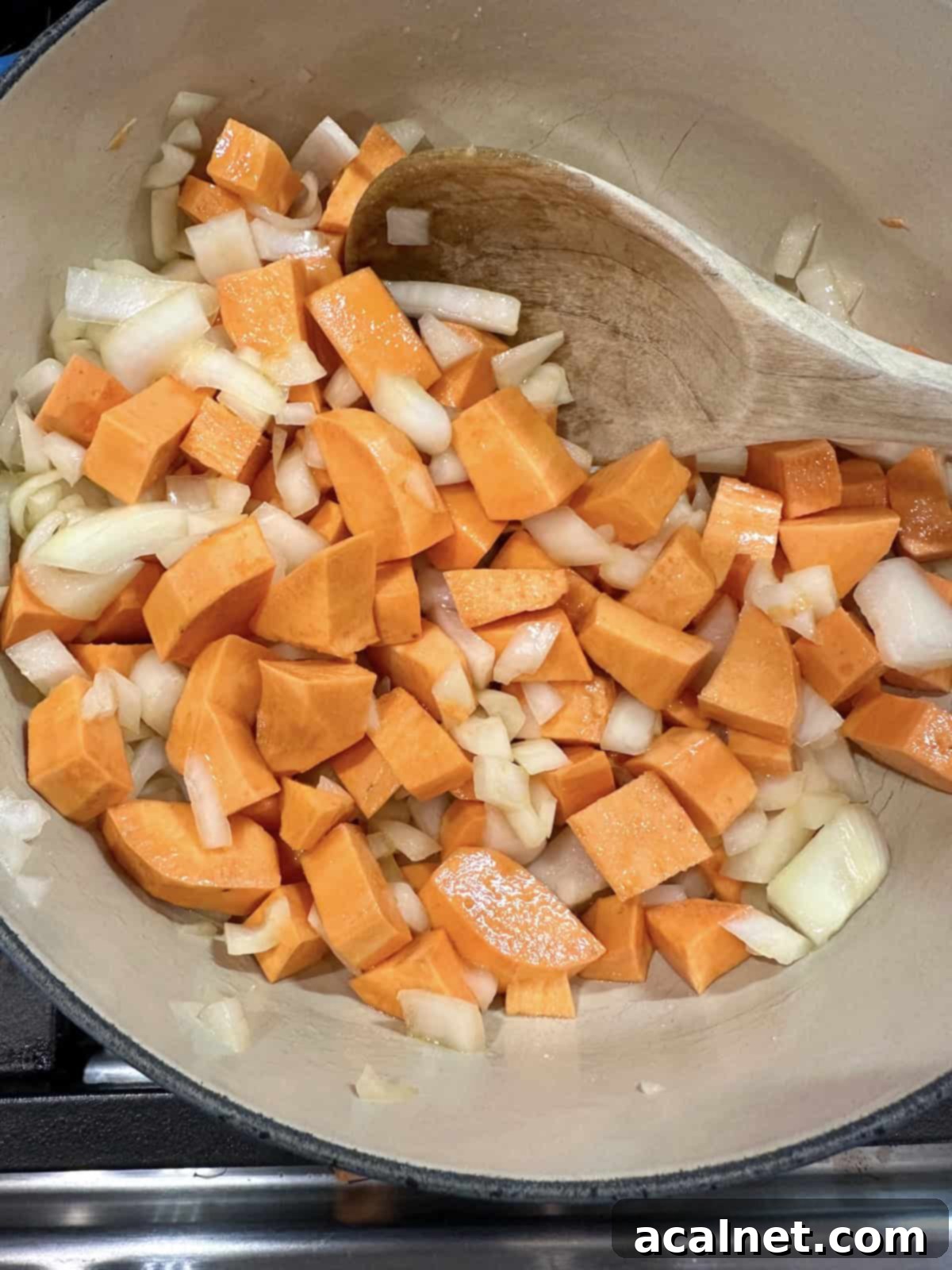 Diced sweet potatoes and onions being sautéed in golden olive oil in a large pot on the stove, releasing their aromatic flavors.