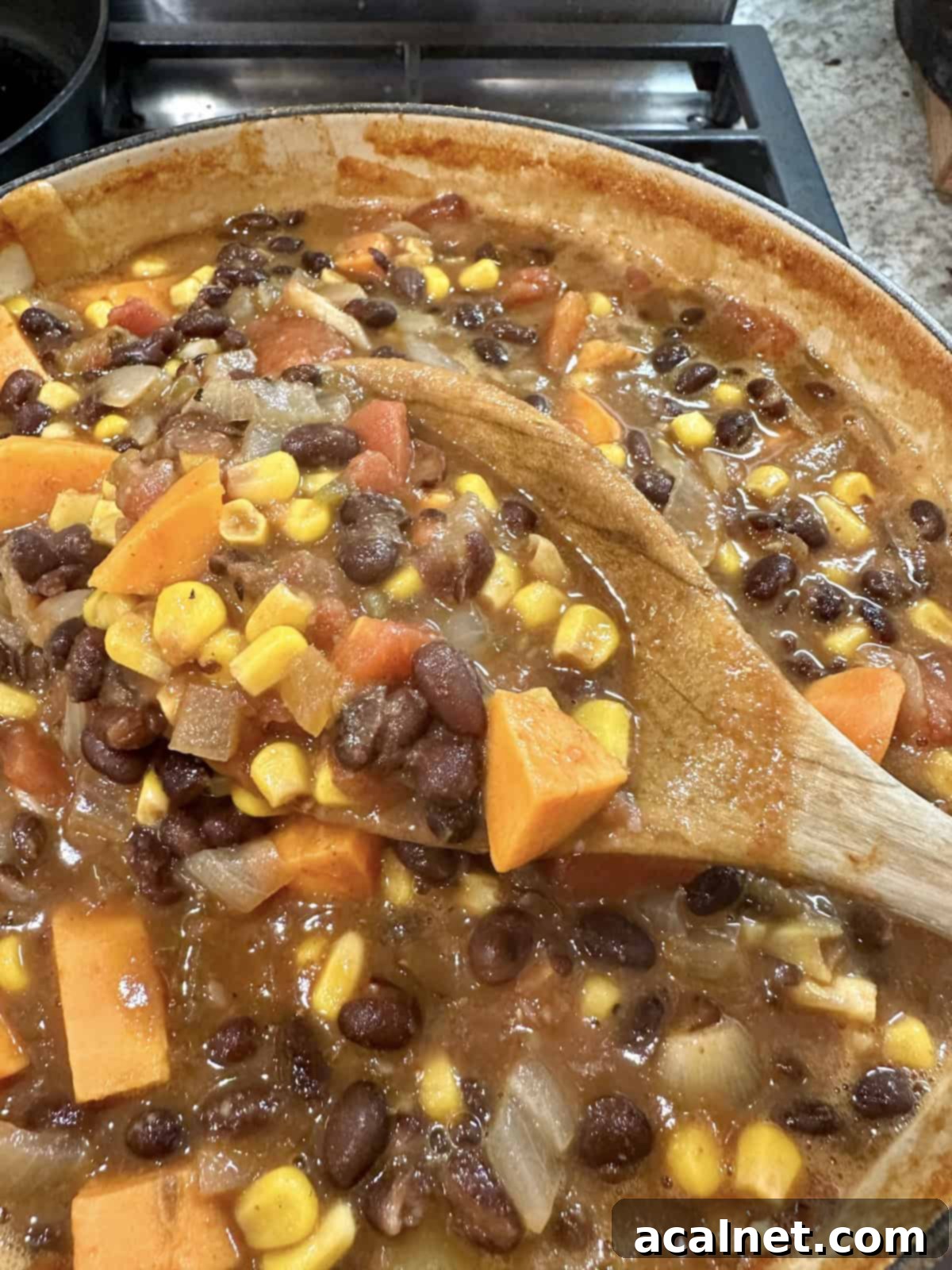 A spoon dishing up a generous serving of vibrant Black Bean Sweet Potato Soup from a large pot, showcasing its rich texture and colorful ingredients.