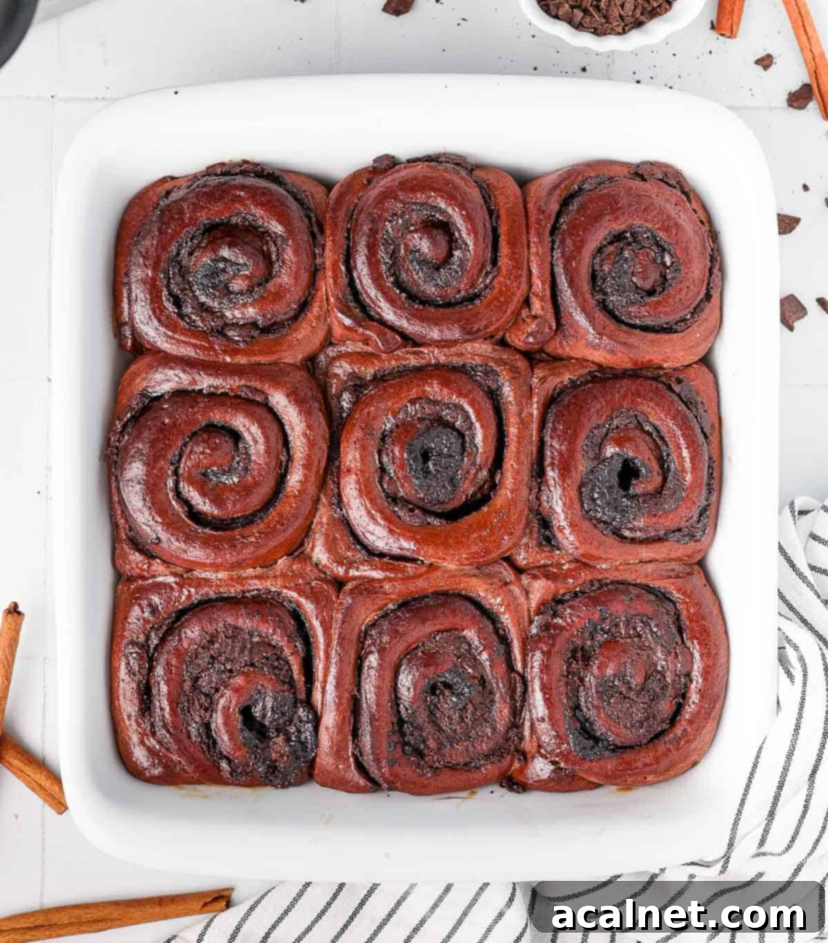 Nine freshly baked triple chocolate cinnamon rolls arranged closely in a square baking pan, ready for frosting.