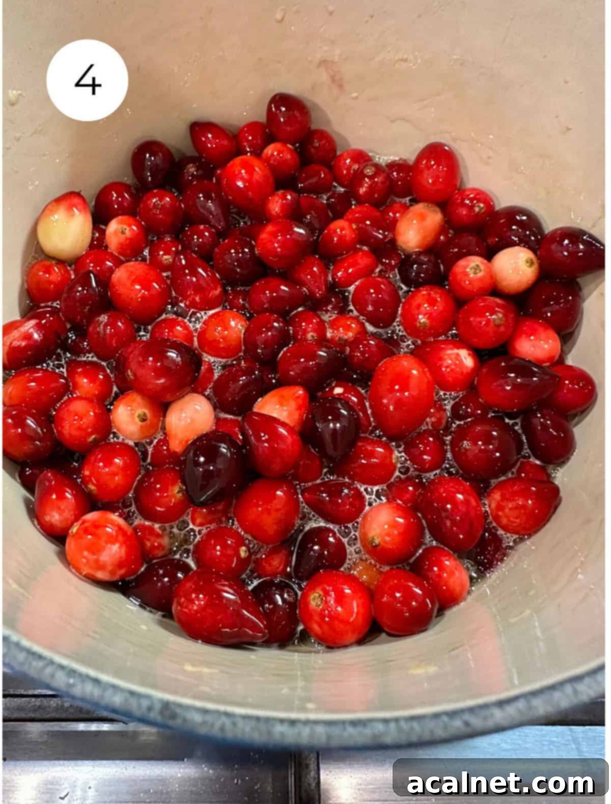 Fresh cranberries with liquid ingredients in a pan on the stove.
