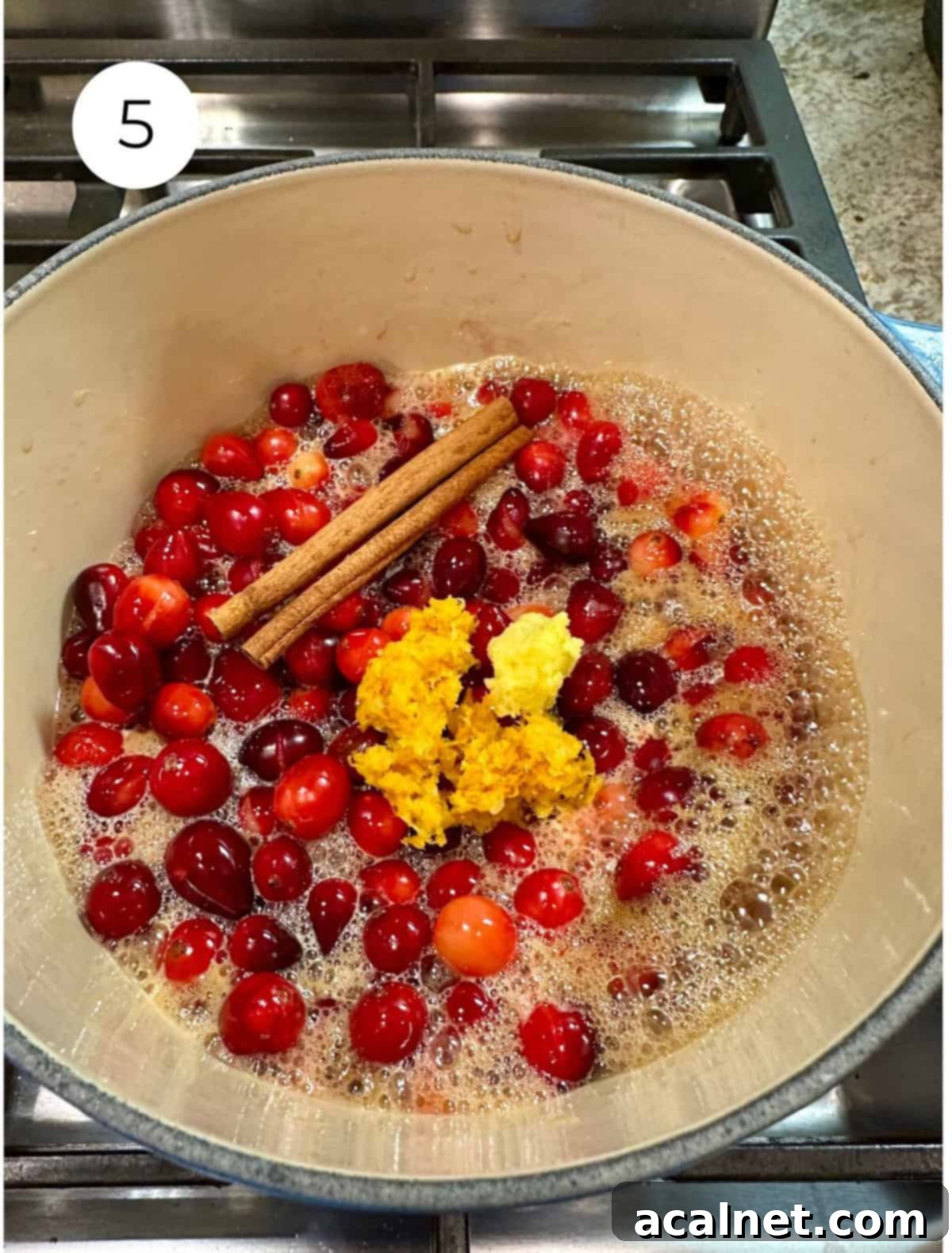 Cranberries with orange zest and cinnamon sticks in a pan on the stove.