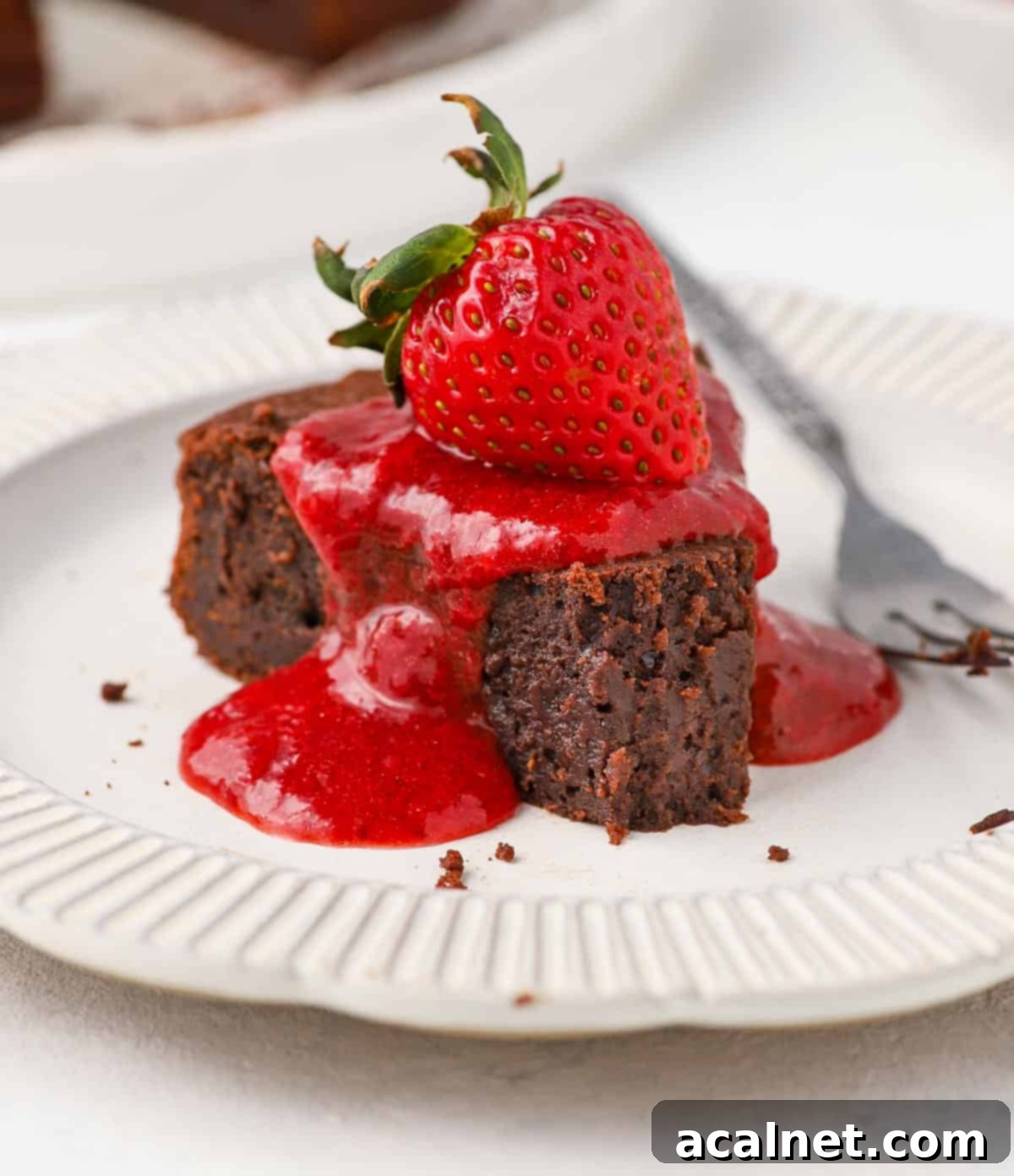 Sauce poured over a slice of chocolate cake and topped with a strawberry.