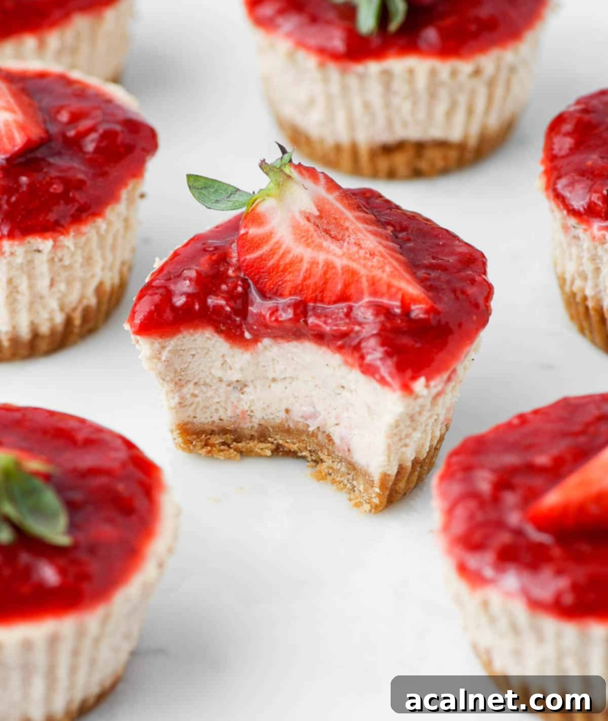 A mini strawberry cheesecake with a bite taken out, showcasing the creamy filling and crisp crust, resting on a marble platter.