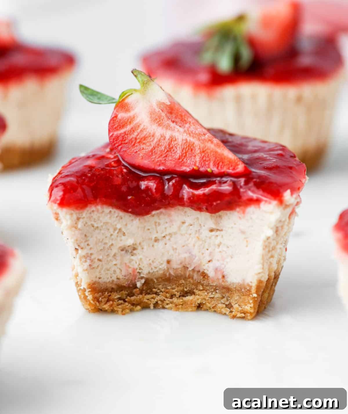 Close up on a mini strawberry cheesecake sliced in half, revealing the creamy strawberry filling and cookie crust texture.