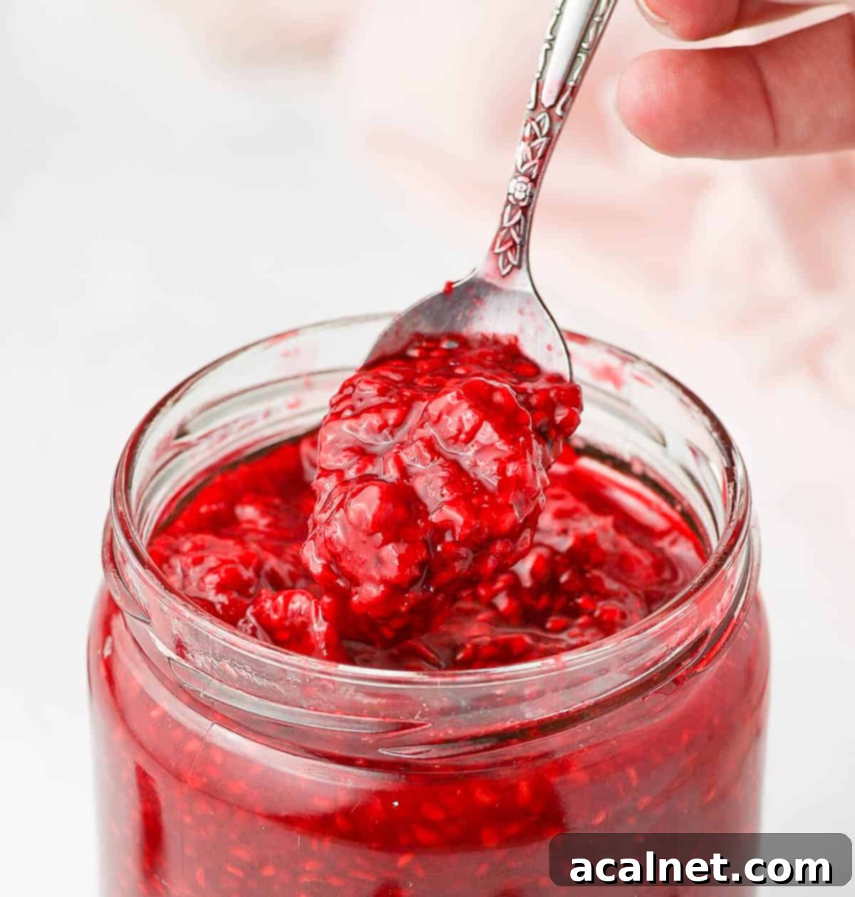 Easy 3 Ingredient Raspberry Compote 5 Close up shot of raspberry compote in a jar, with a spoon lifting some of the thick, textured sauce.