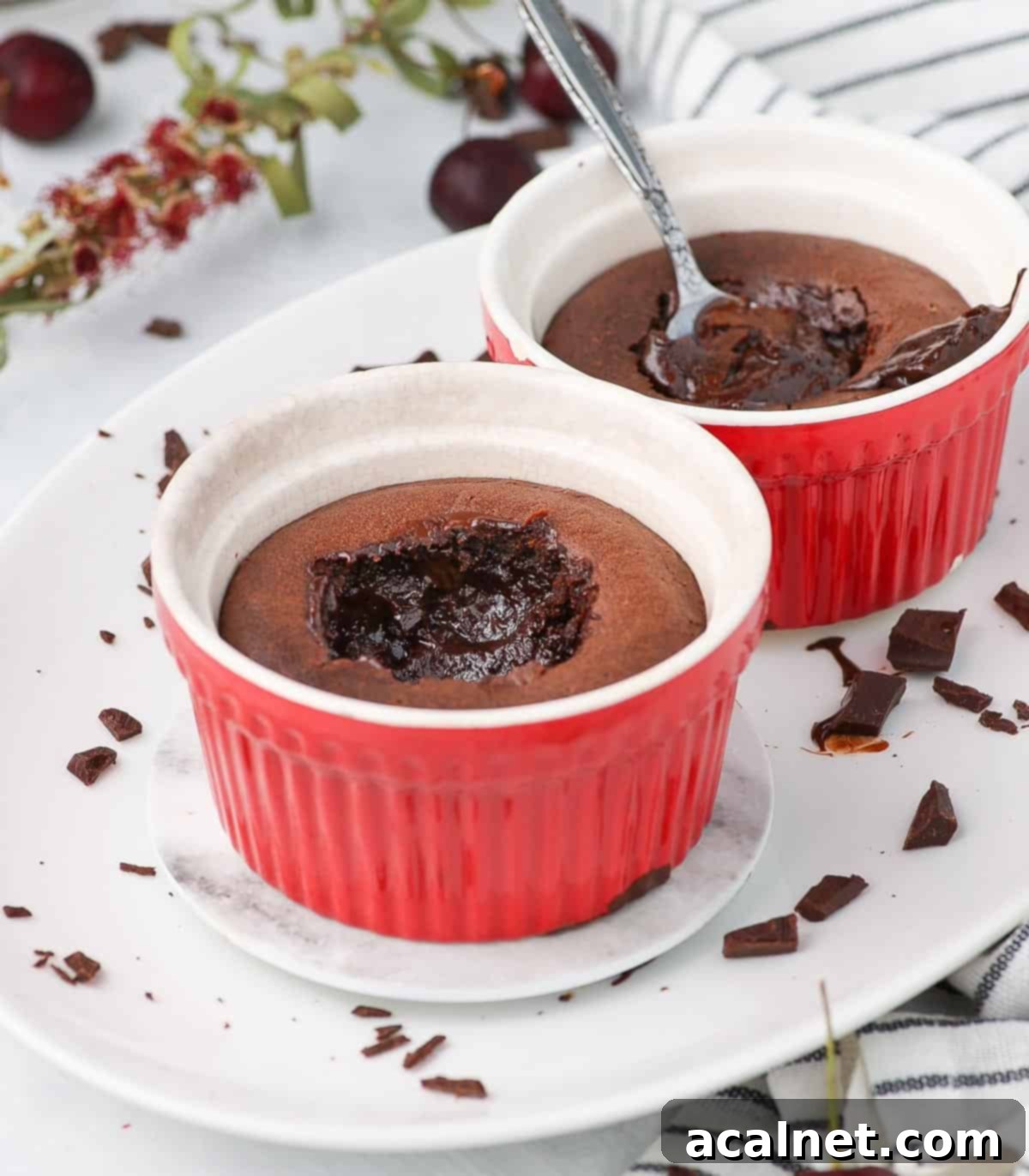 Two vibrant red ramekins, each containing a chocolate fondant cake, are elegantly presented on an oval white plate, ready to be enjoyed.