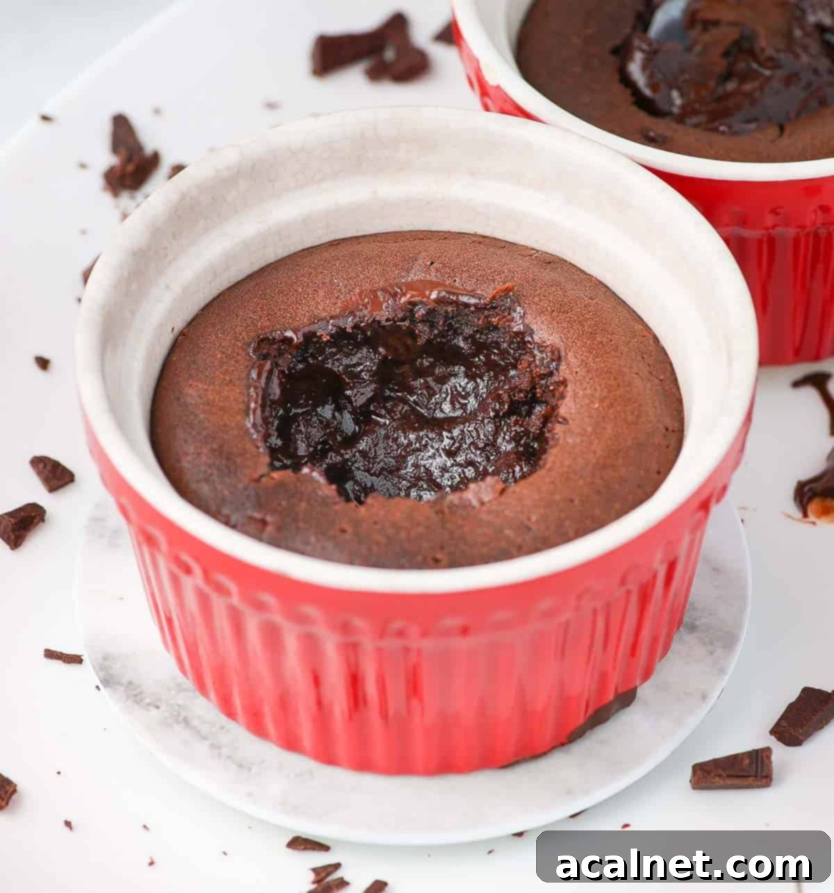 A chocolate cake in a red ramekin with a spoon digging into its molten, gooey center, showing the rich dark chocolate.