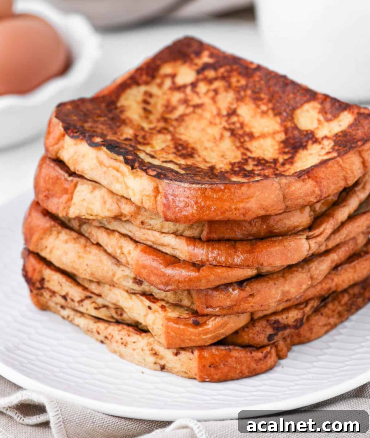 A magnificent stack of golden brioche French toast slices, perfectly cooked and waiting for delicious toppings, presented on a pristine white plate.