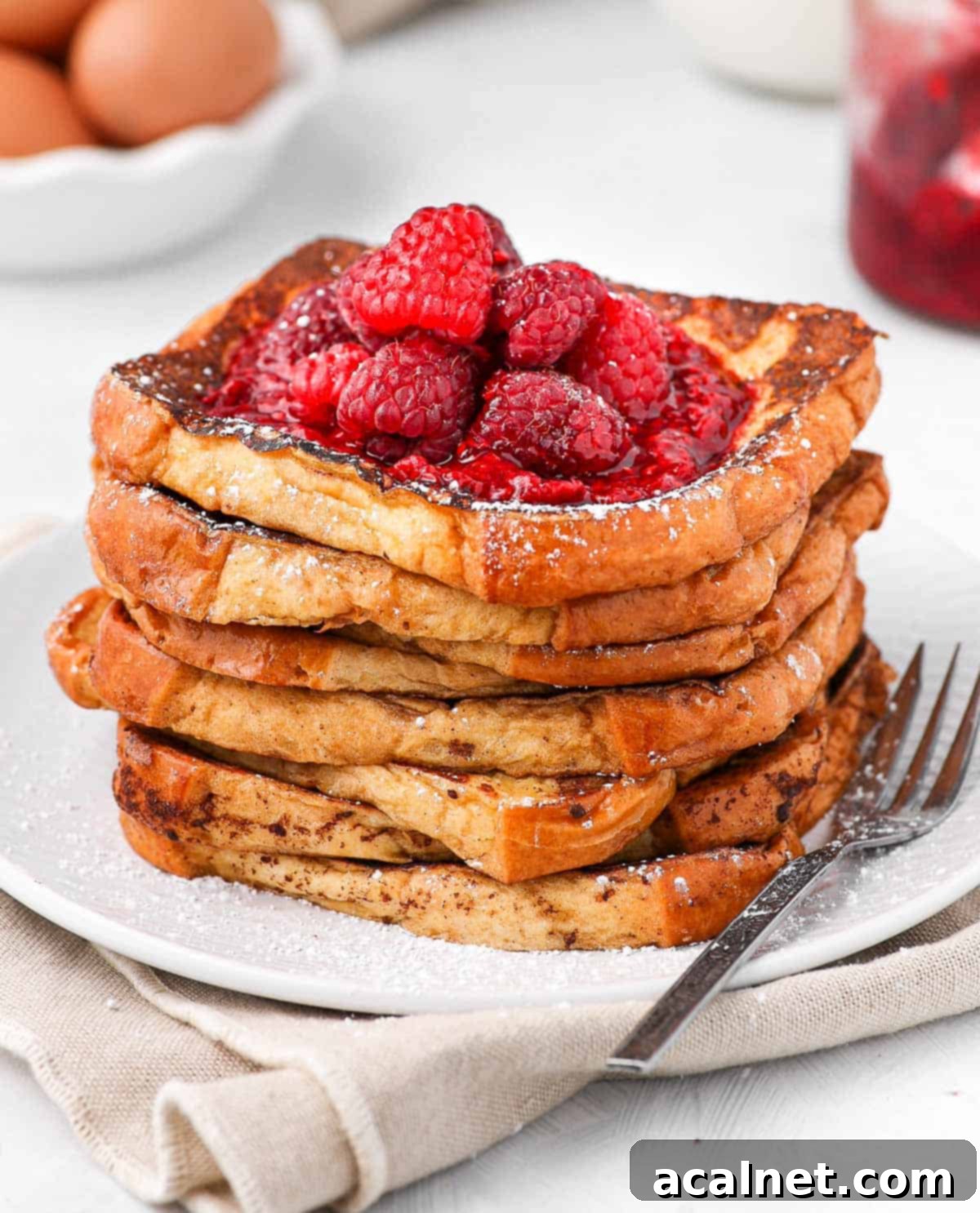 A stack of brioche French toast slices, beautifully topped with a vibrant raspberry compote and fresh raspberries, creating a tempting breakfast presentation.