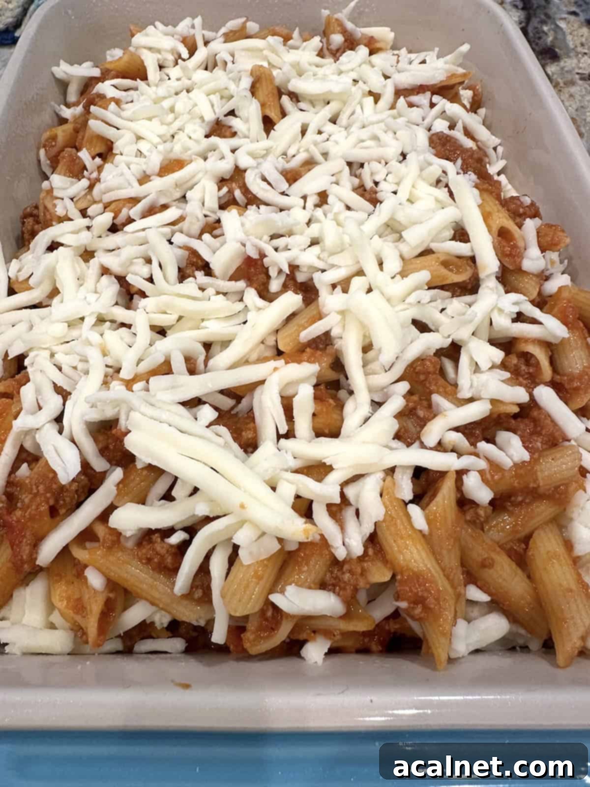 Unbaked pasta, sauce, and meat in a baking dish with the remaining mozzarella cheese sprinkled on top.