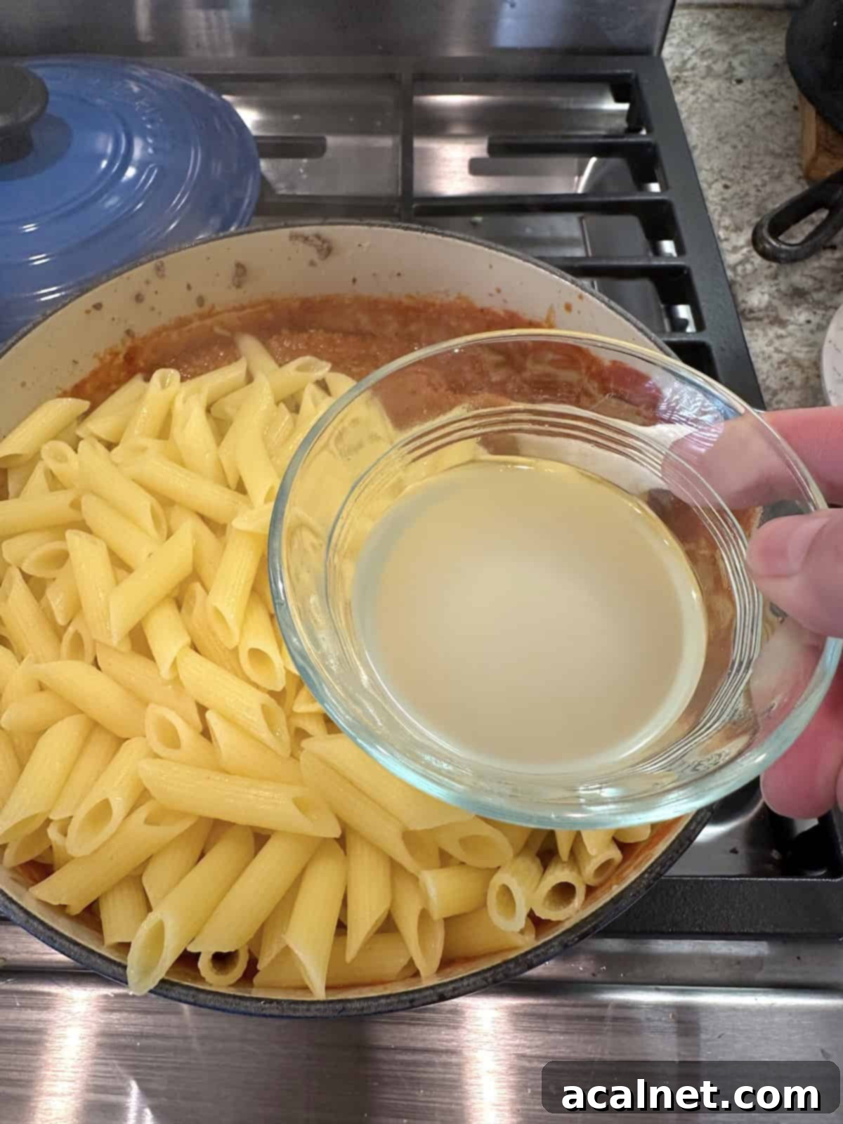 Cooked pasta and sauce for lazy lasagna in a pan with a cup of pasta water being added.