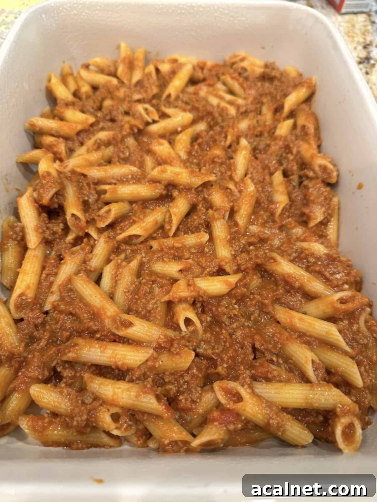 First layer of pasta, meat, and sauce spread evenly in a 9x13 inch baking dish.