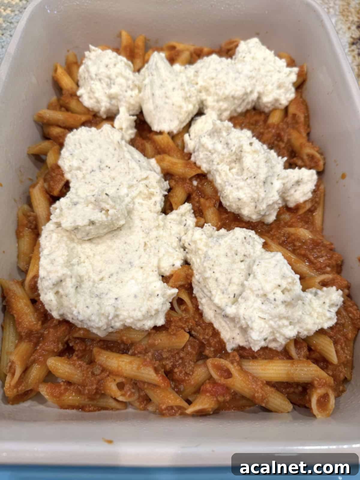 Unbaked lazy lasagna in a baking dish with the creamy ricotta cheese mixture spooned on top of the first pasta layer.