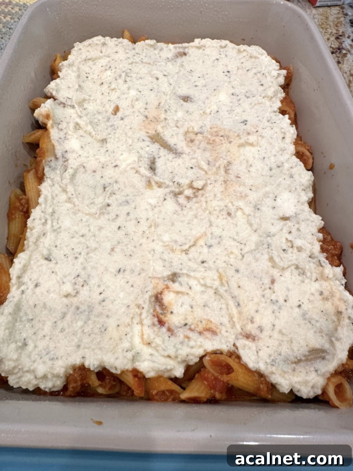 Ricotta cheese spread evenly over a layer of pasta, meat, and sauce in a baking dish.