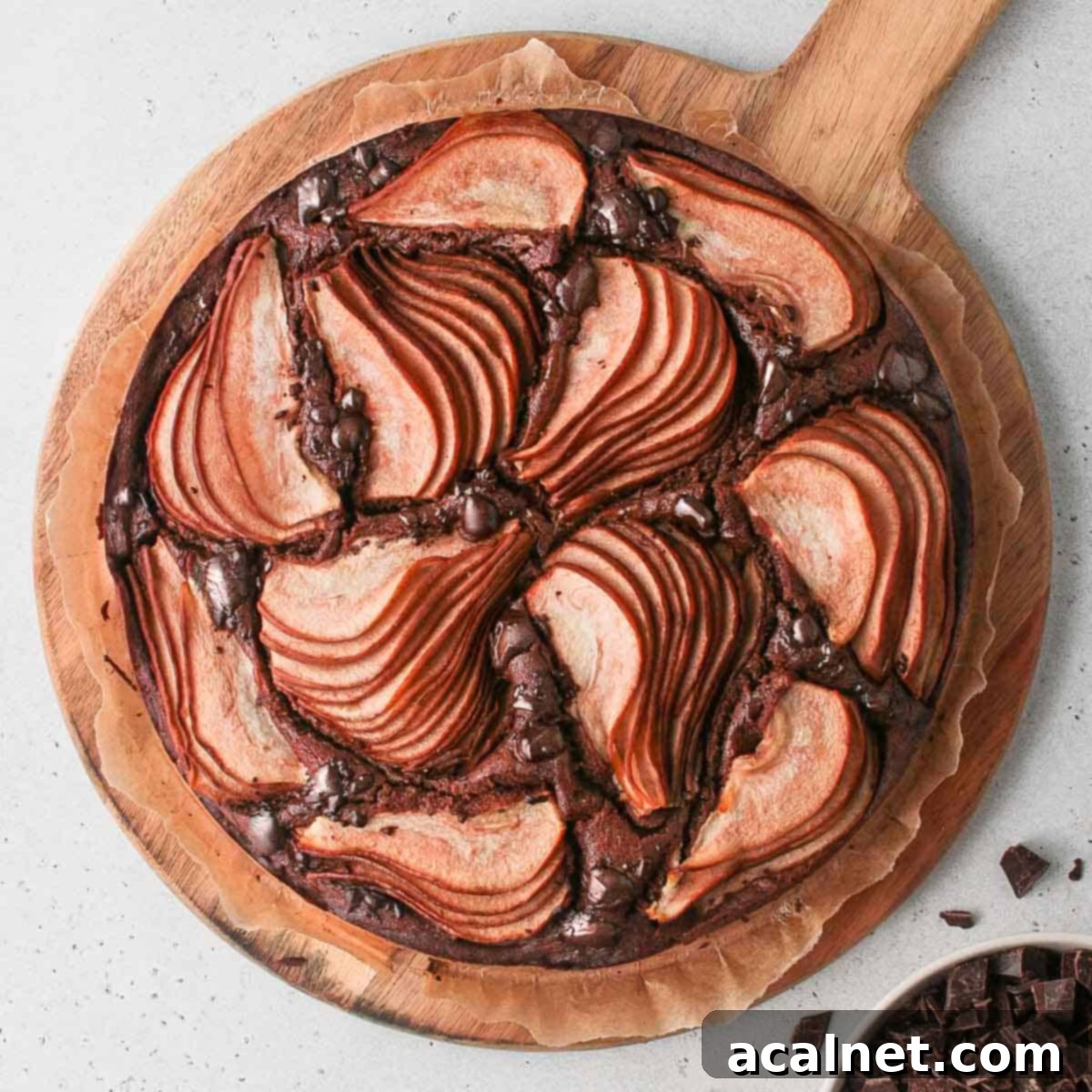 A beautifully baked Chocolate Pear Cake, seen from above on a round wooden board, showcasing the artfully arranged pear slices and melted chocolate.