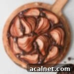 A beautifully baked Chocolate Pear Cake, seen from above on a round wooden board, showcasing the artfully arranged pear slices and melted chocolate.