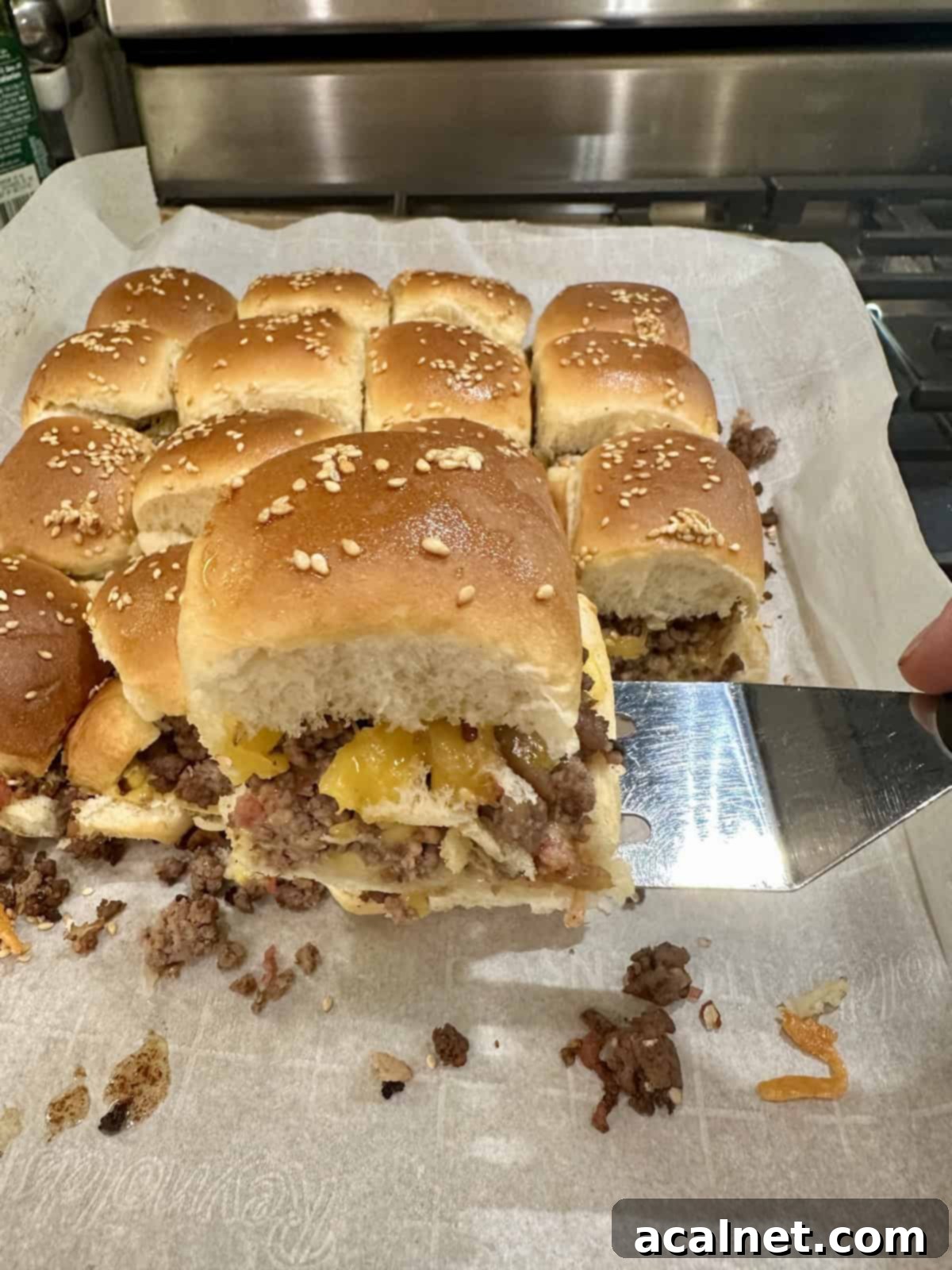 A spatula serving a cheeseburger slider from a baking pan on the stovetop.