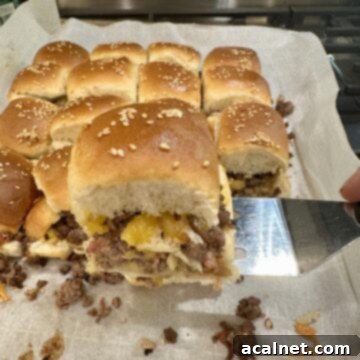 A spatula serving a cheeseburger slider from a baking pan on the stovetop.